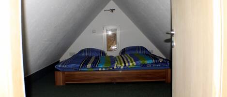A small, triangular attic bedroom with a single bed, a window, and a door.