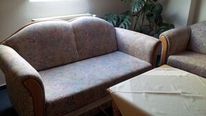 Een woonkamer met een bank met bloemenprint, een houten bijzettafeltje en een potplant.
