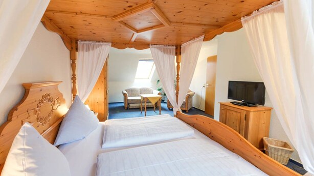 Een slaapkamer met een houten plafond, een bed met witte lakens, een televisie op een houten kast en een stoel in de hoek.