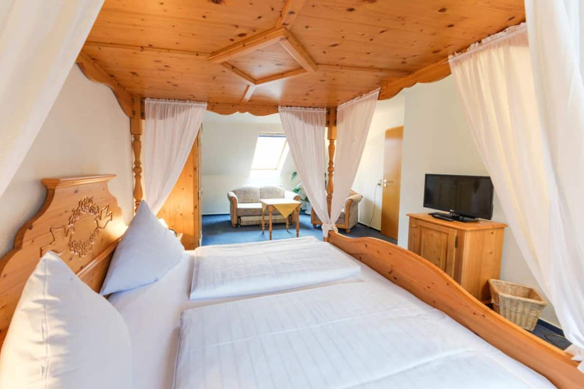 Un dormitorio con techo de madera, una cama con sábanas blancas, un televisor sobre un mueble de madera y una silla en la esquina.