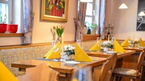 Een restaurant met houten tafels en stoelen, gele servetten en een vaas met bloemen op elke tafel.