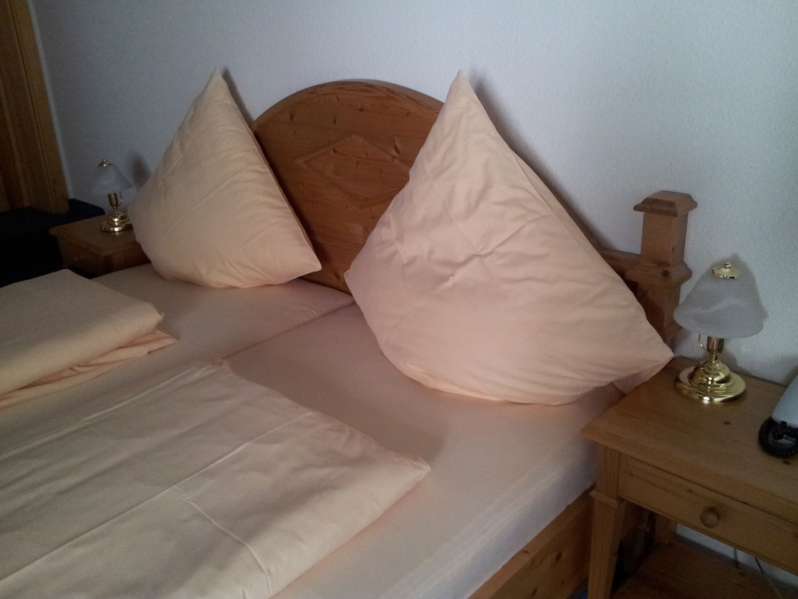 A neatly made bed with a wooden headboard, two bedside lamps, and a wooden nightstand.