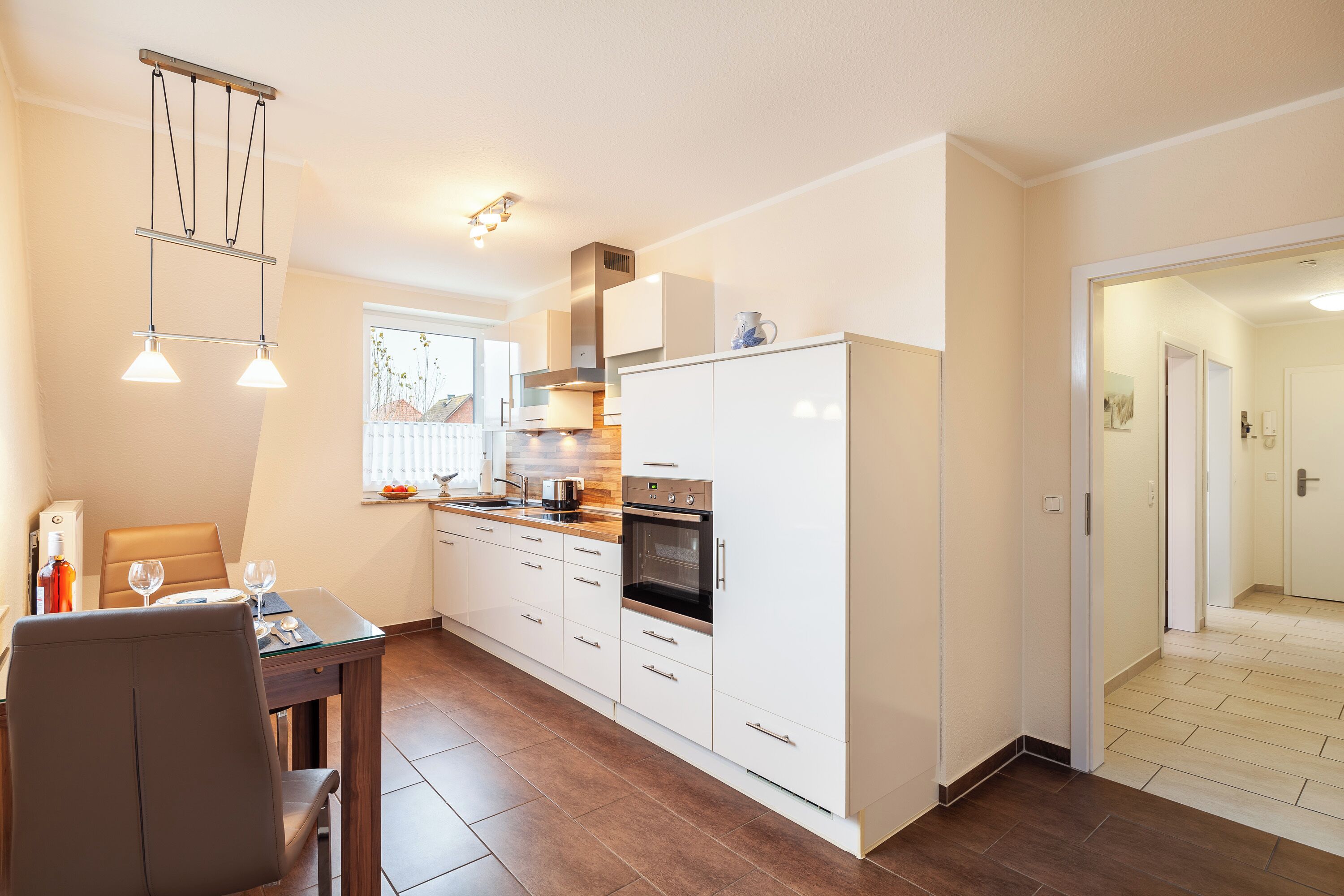 A modern kitchen with white cabinets, a built-in oven, and a dining area with a table and chairs.