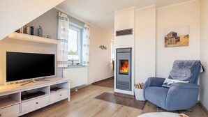Ein modernes Wohnzimmer mit Flachbildfernseher, Kamin, bequemen Sessel und Bücherregal.