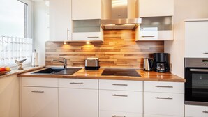 Eine moderne Küche mit weißen Schränken, einer Holz-Spritzschutzwand, einer Edelstahl-Dunstabzugshaube, einem Spülbecken, einem Toaster und einer Kaffeemaschine.