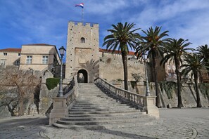 A historic stone staircase leading to a fortified tower with a flag, palm trees, and traditional buildings in the background. - Hostel Korcula (Korcula)