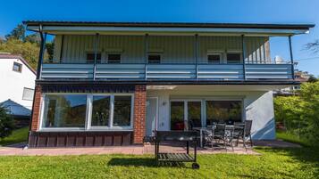 A two-story house with a balcony, large windows, and a patio area with outdoor furniture.