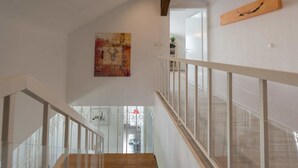 Un escalier avec des finitions en bois et des rampes en verre, menant à une pièce dotée d’une porte blanche et d’un tableau au mur.
