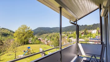 A balcony with a view of a green landscape, a playground, and houses in the distance.