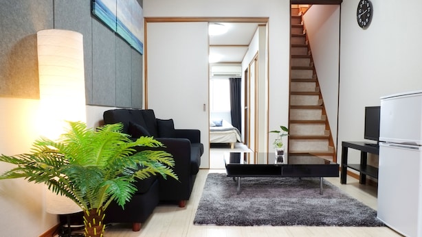 Una sala de estar moderna con un sofá, una mesa de centro, una planta en maceta, una lámpara y una escalera que lleva a otra habitación.
