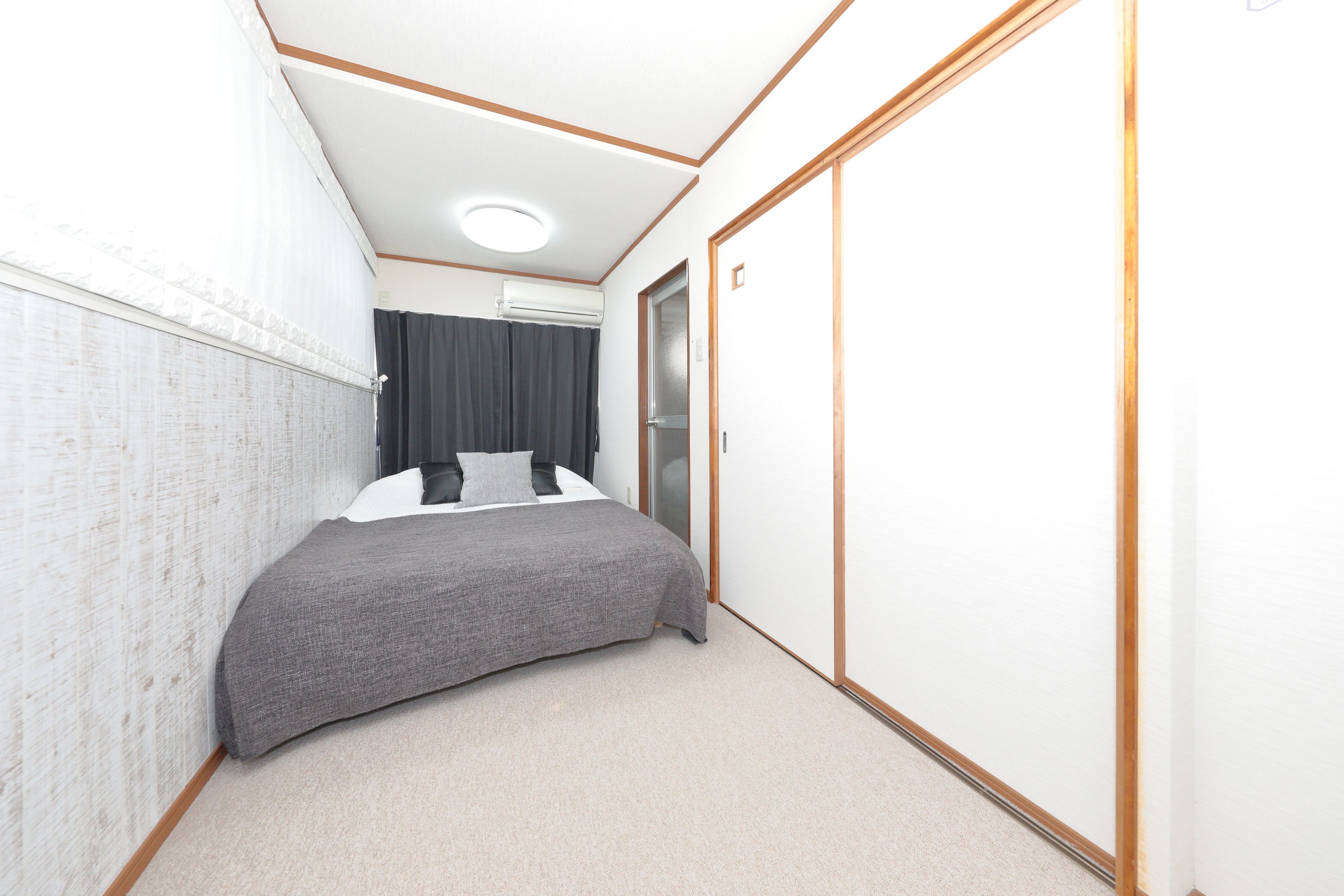 A bedroom with a bed, a wardrobe, a ceiling light, and a window with curtains.