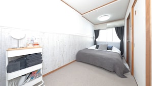 Un dormitorio con cama, mesita de noche, estante en la pared con toallas y ventana con cortinas.