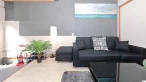 Una sala de estar moderna con un sofá negro, una planta pequeña en maceta, un extintor y un cuadro de una playa en la pared.