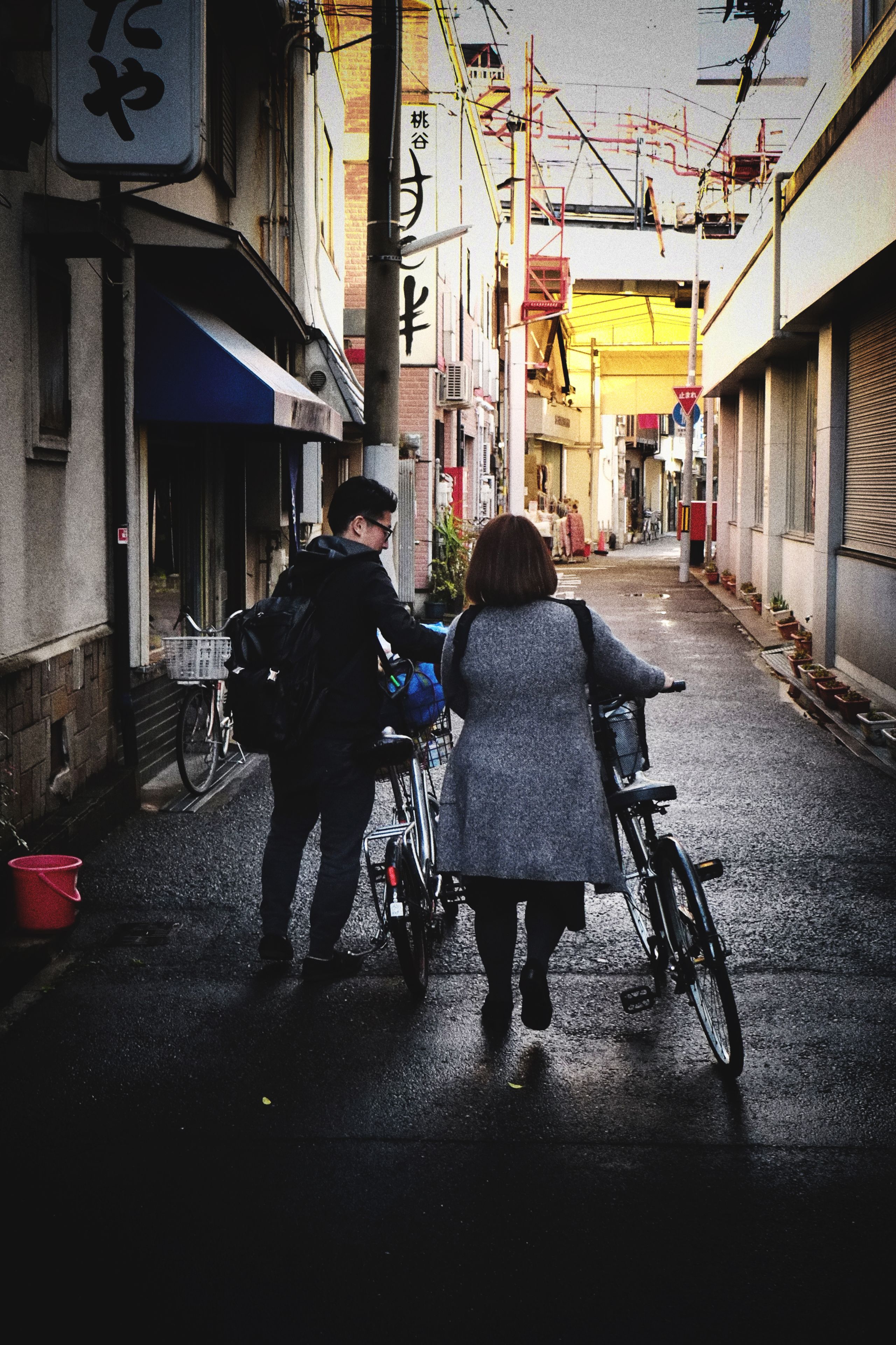 A narrow alley with buildings on either side, a bicycle, and a person pushing a bicycle.
