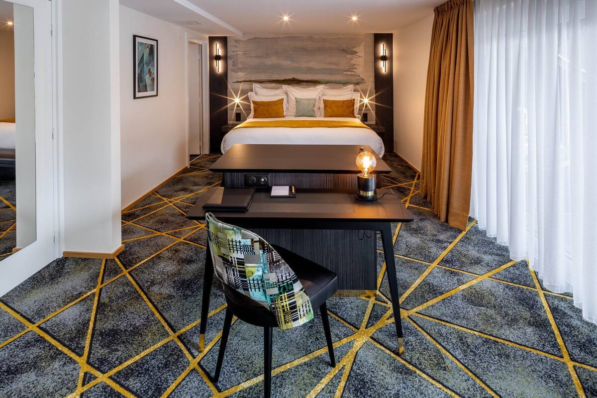A hotel room with a bed, a desk, a chair, and a nightstand.