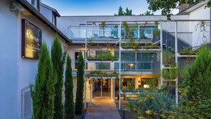 Un hotel moderno con fachada de vidrio, mobiliario exterior y un jardín cuidado.