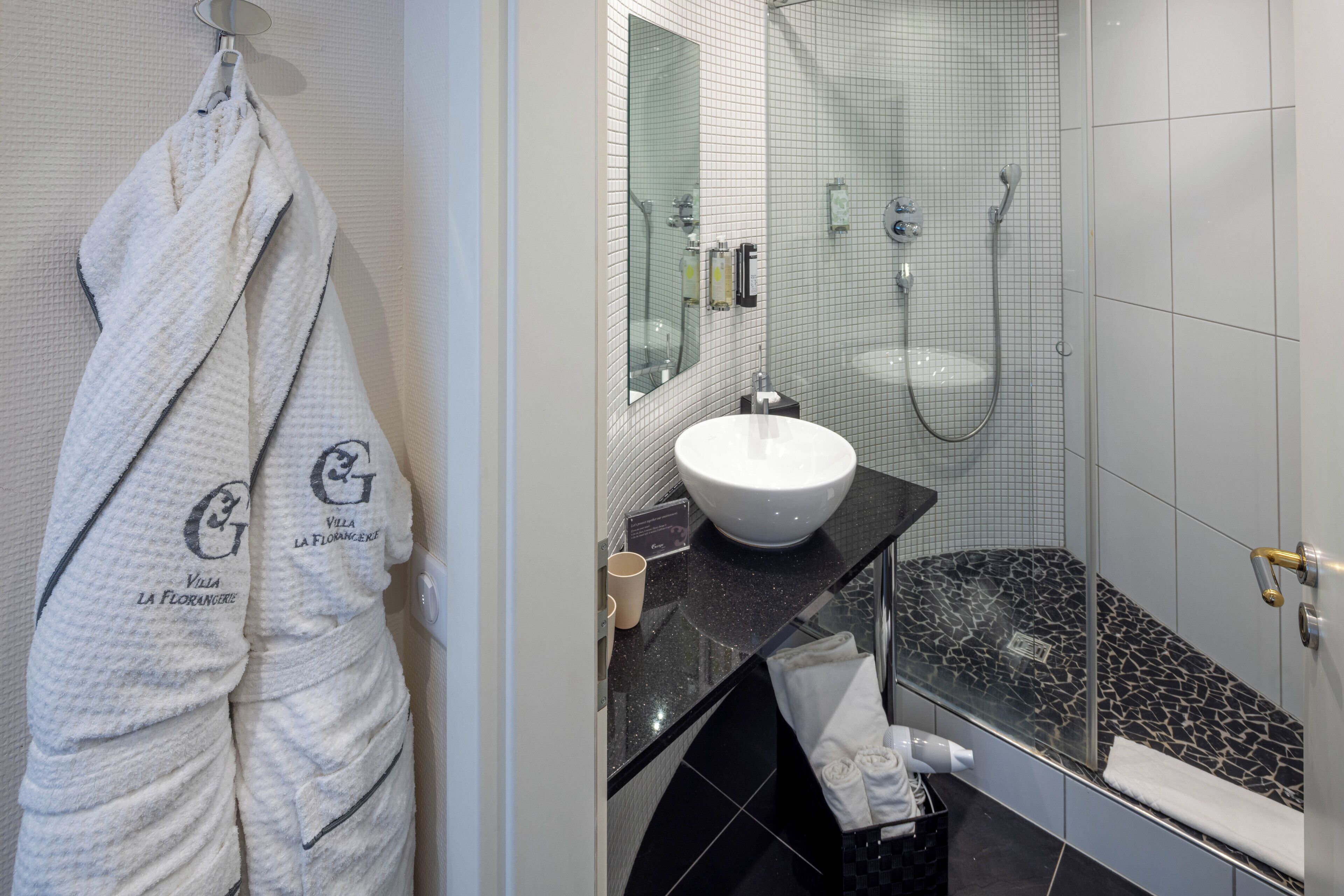 Une salle de bain avec un lavabo blanc, un miroir, une douche et un porte-serviettes avec des peignoirs.