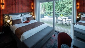 Una habitación de hotel moderna con una cama grande, un balcón con mobiliario exterior y una pared con diseño de ladrillo.