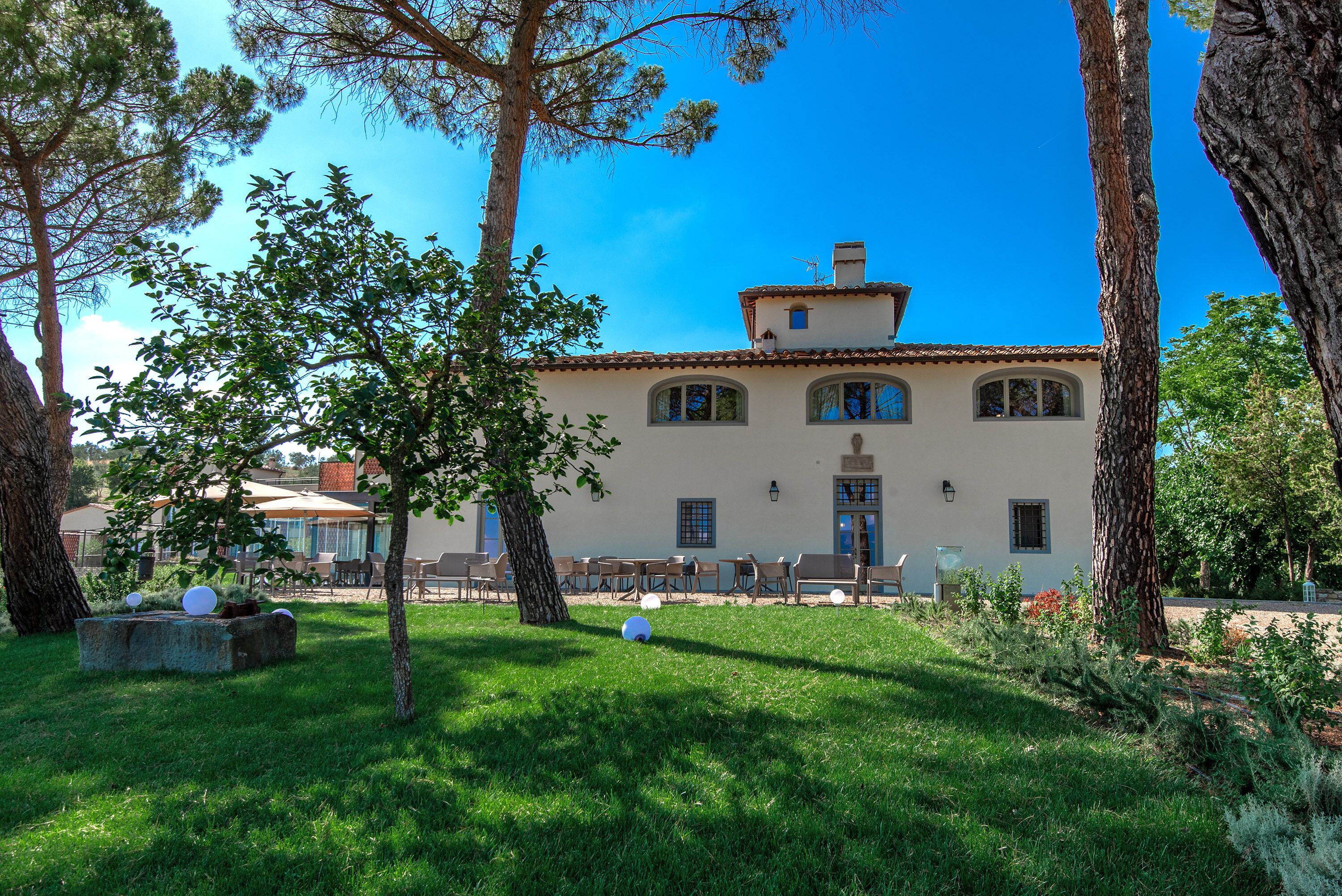 A building with a tiled roof, a central entrance, and a garden with trees and outdoor seating.