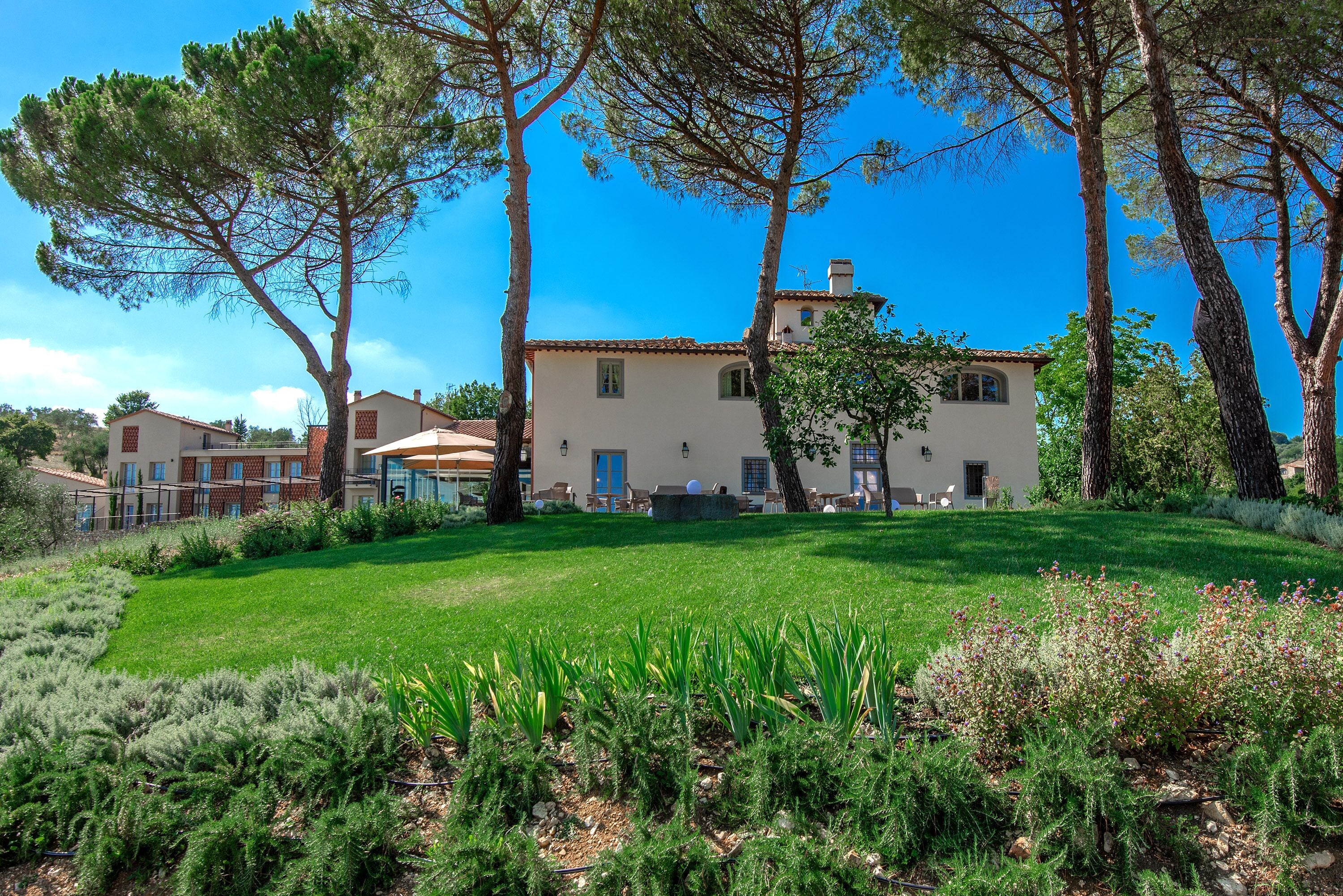 A large building with a garden in front, surrounded by trees.