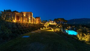 Une belle maison d’habitation, bien éclairée au crépuscule, avec une piscine, un chemin de pierre et une vue sur le paysage environnant.