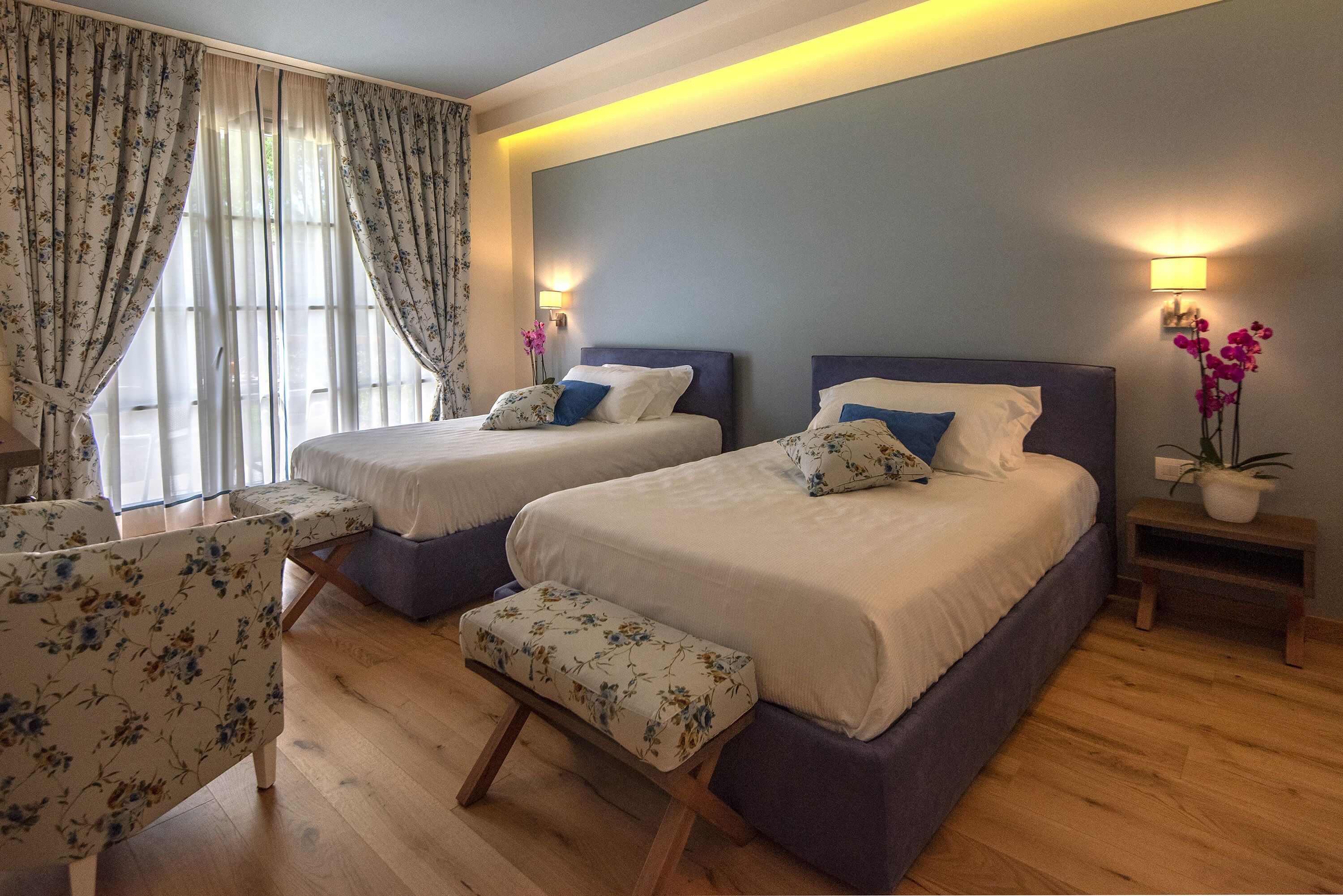 A hotel room with two beds, a chair, and a bench.