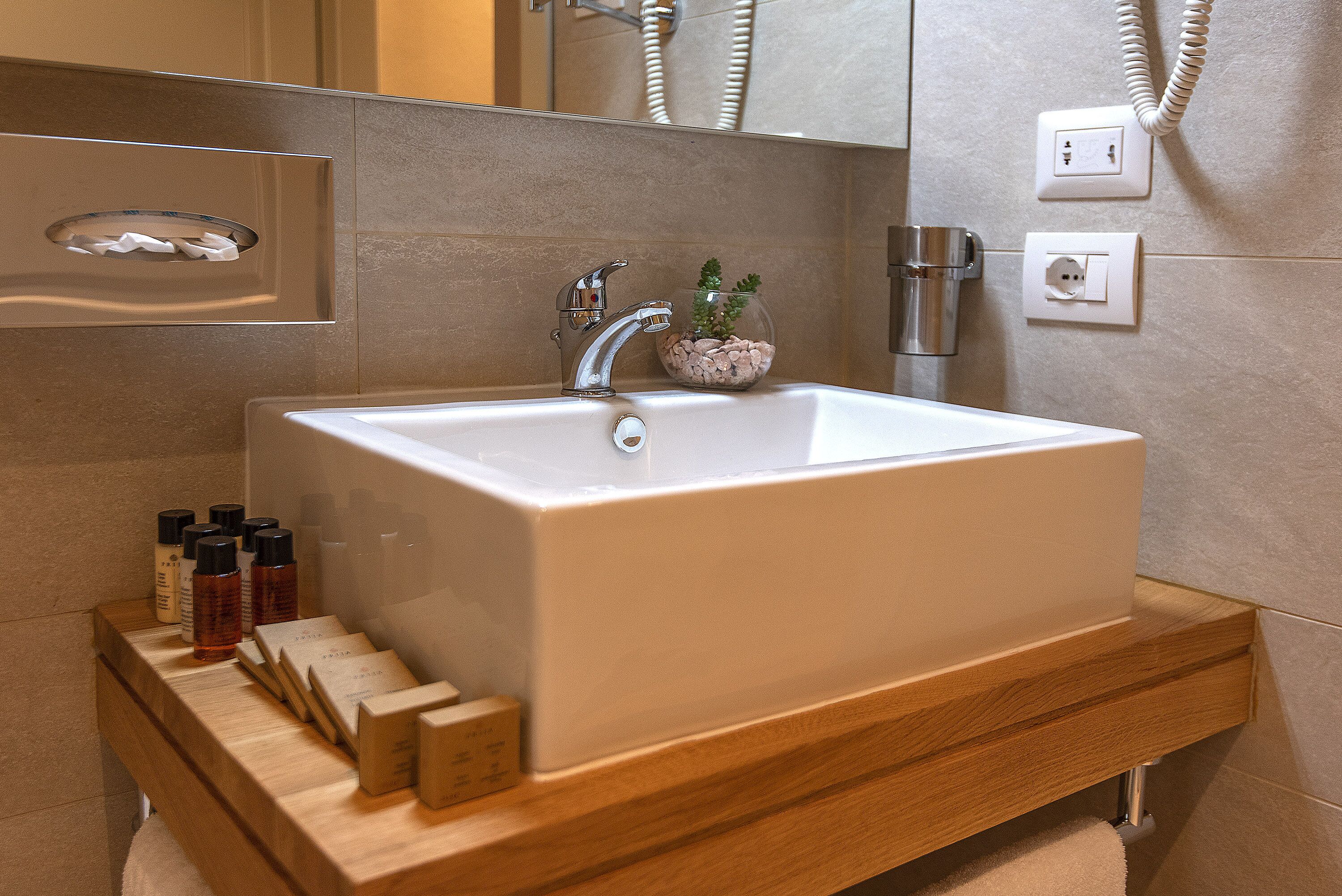 A modern bathroom with a rectangular sink, wooden vanity, and a glass container with decorative stones.