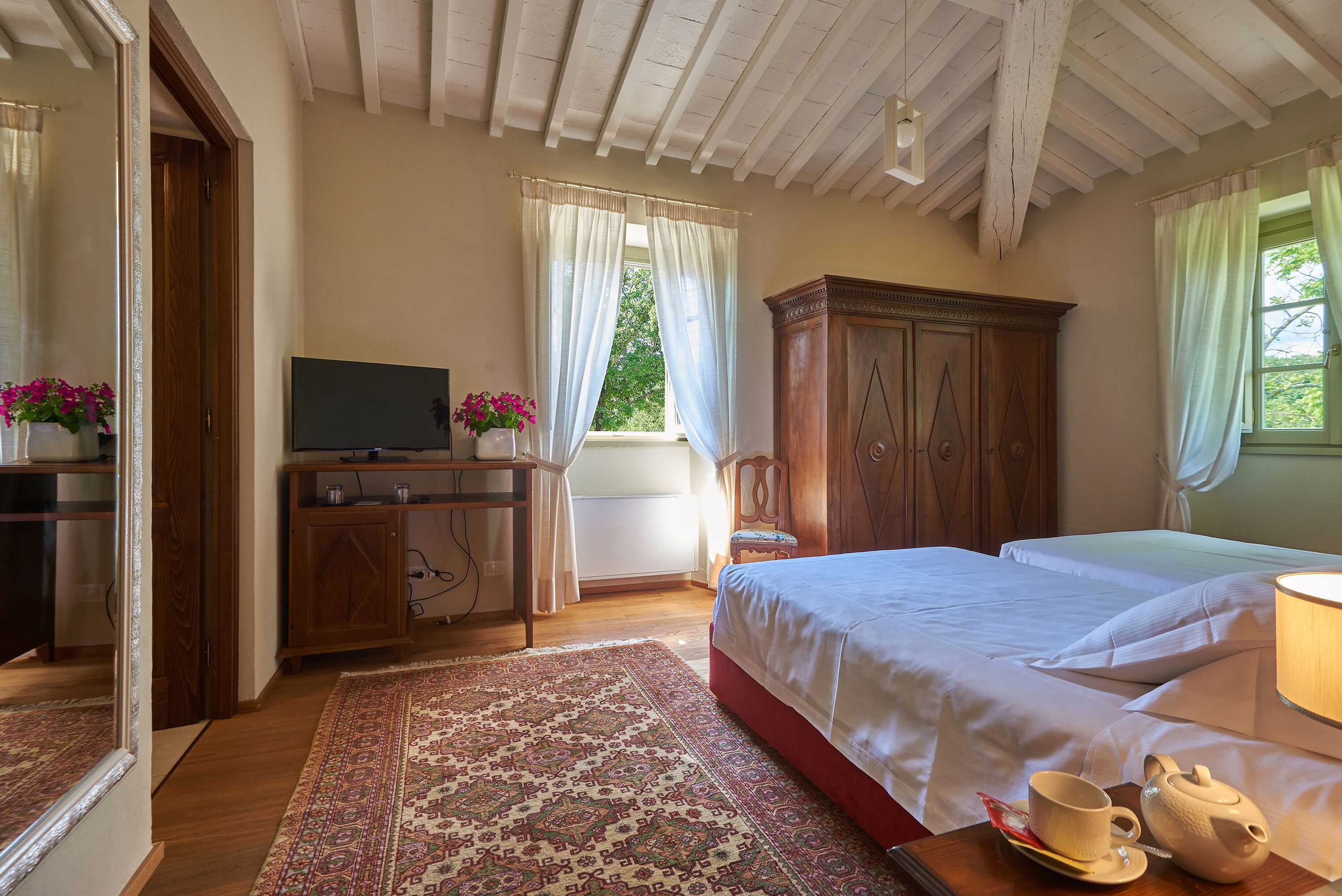 Een slaapkamer met een groot bed, een houten kast, een televisie en een raam met gordijnen.