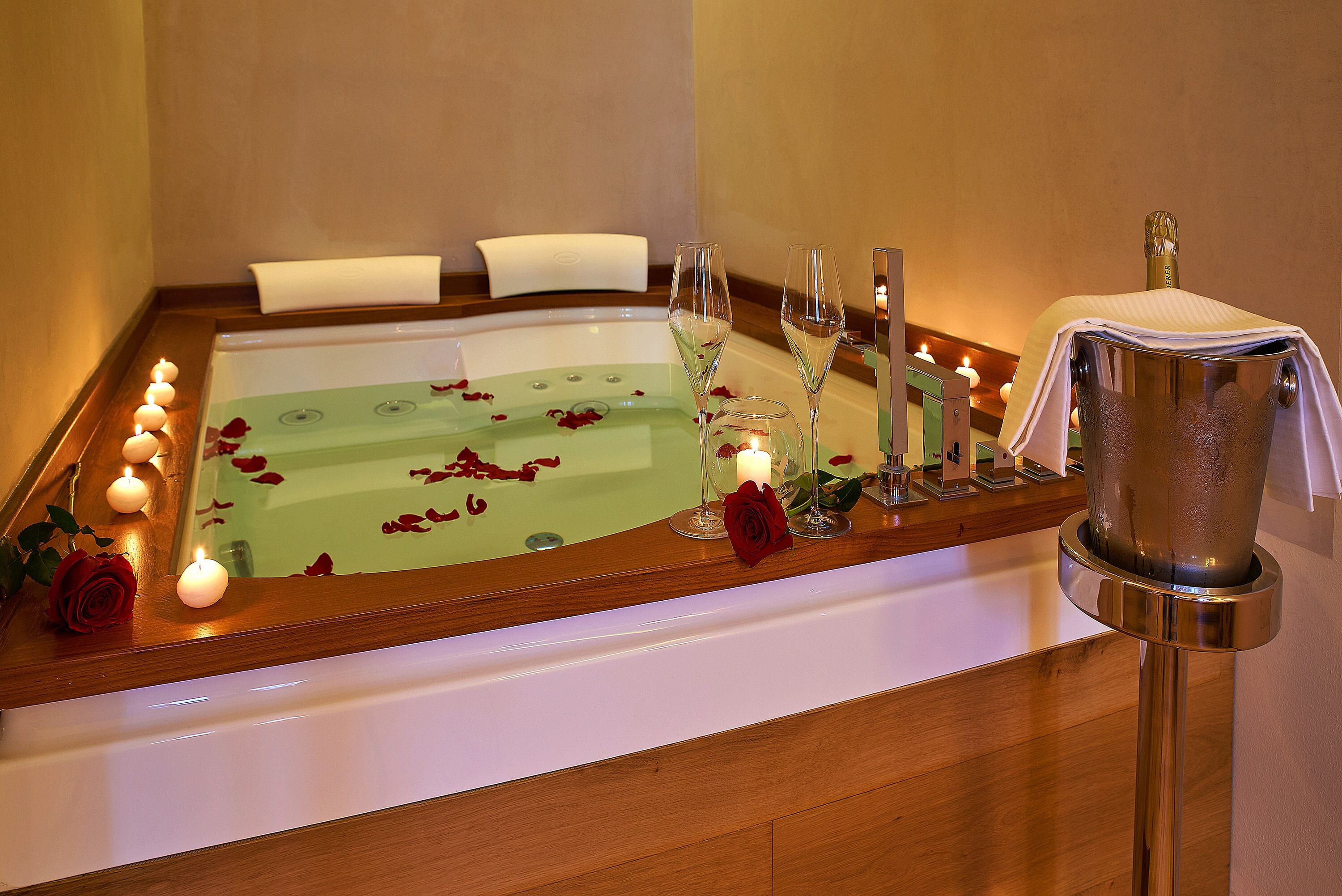A bathtub with rose petals, candles, and champagne glasses.