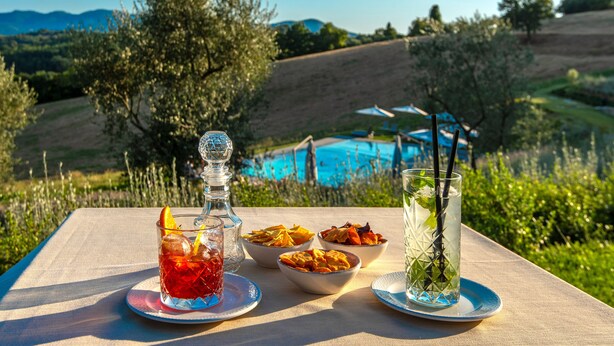 Une table avec des boissons et des en-cas, donnant sur une piscine et des collines.