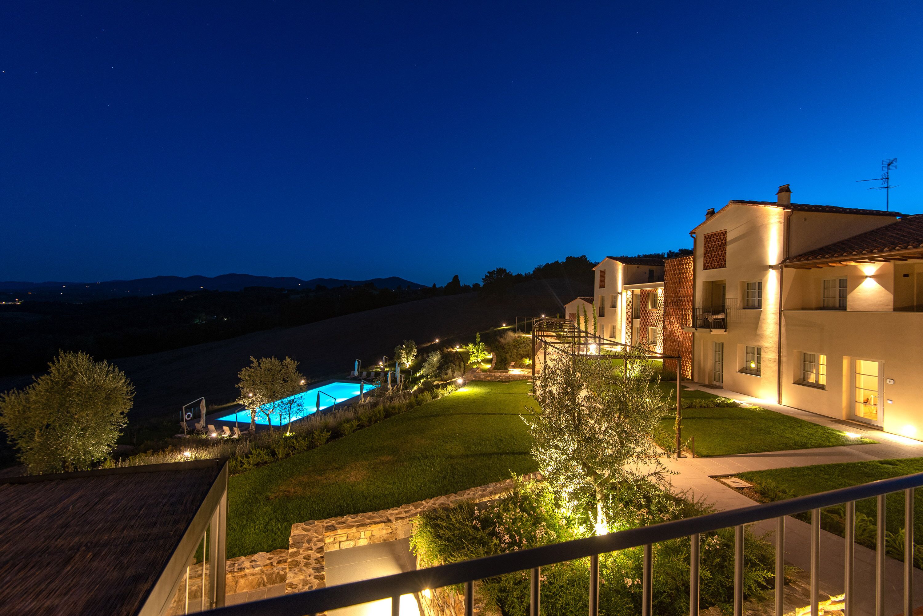 A residential property at dusk with a swimming pool, well-lit pathways, and a view of distant hills.