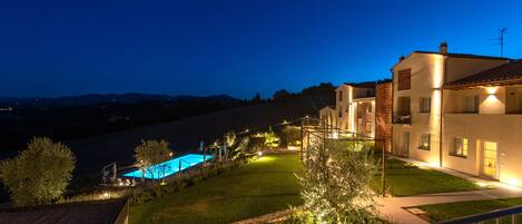 A residential property at dusk with a swimming pool, well-lit pathways, and a view of distant hills.