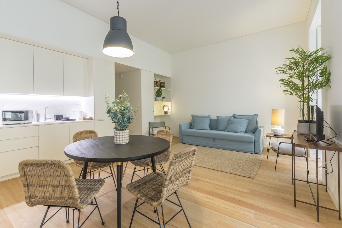 A modern kitchen with white cabinets, a dining table with wicker chairs, a blue sofa, and a potted plant.