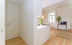 A modern, well-lit room with a wooden floor, a white door, a small table with a plant, a TV on a stand, and a window with natural light. - Free Spirit House Baixa-Chiado (Lisbon)