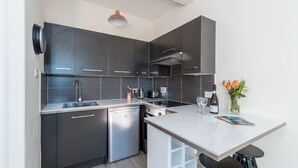 A modern kitchen with dark cabinetry, a built-in dishwasher, and a white countertop. - Silver Lining Charming Meadowbank Flat (Edinburgh)