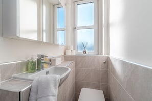 Ein modernes Badezimmer mit Waschbecken, Spiegel und Badewanne. Auf der Ablage liegen Toilettenartikel und ein Fenster mit Blick zum Himmel.