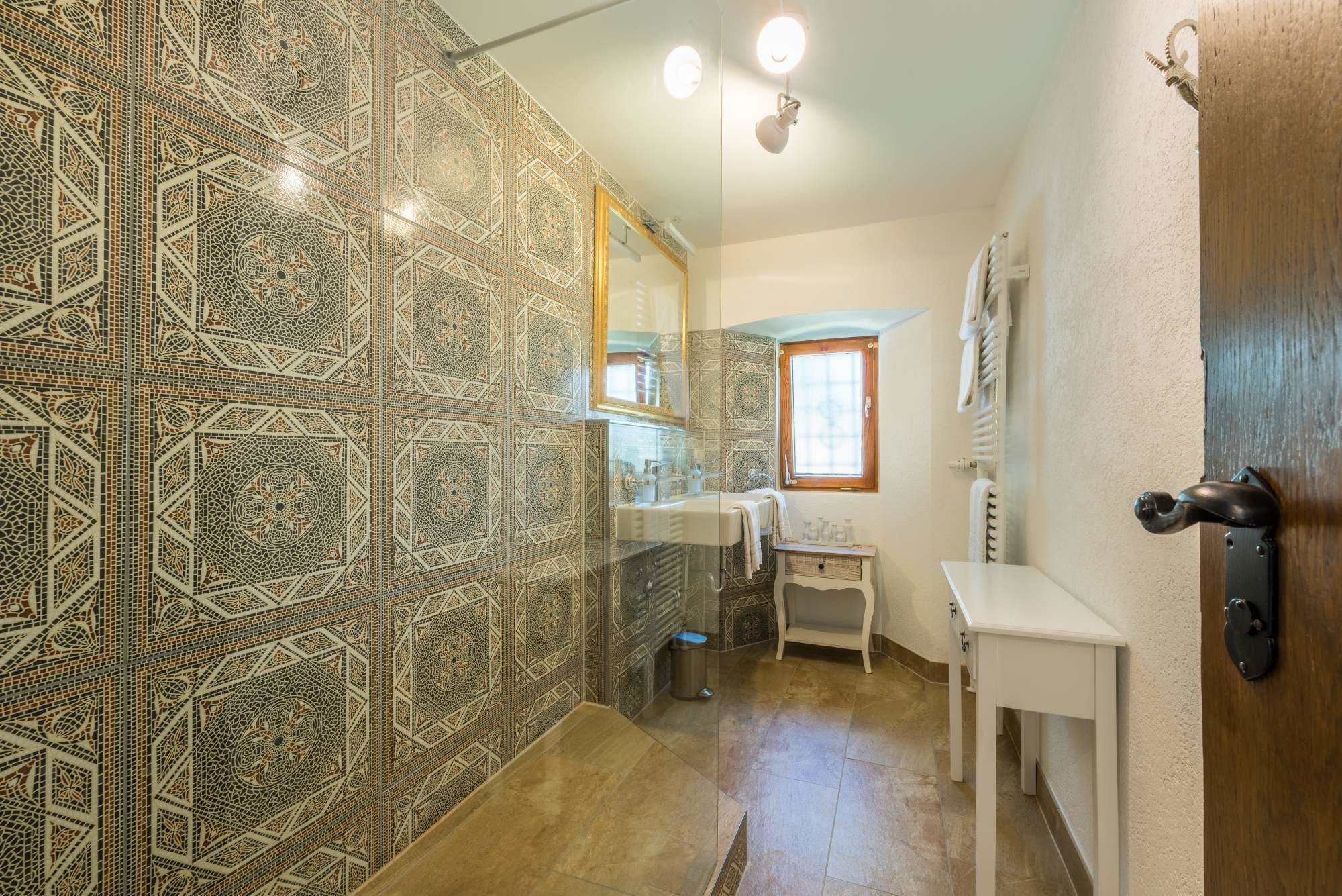 A bathroom with intricate tile patterns, a sink, a mirror, a window, and a door.
