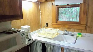 Une cuisine compacte avec des meubles en bois, un four à micro-ondes, un évier et une fenêtre donnant sur l’extérieur.