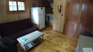 Un espace de vie compact doté d’un plancher en bois, d’un canapé, d’une petite table, d’un réfrigérateur et d’une porte.