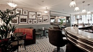 A bar area with a curved counter, framed pictures on the wall, and a seating area with a red sofa and chairs. - Cults Hotel (Aberdeen)
