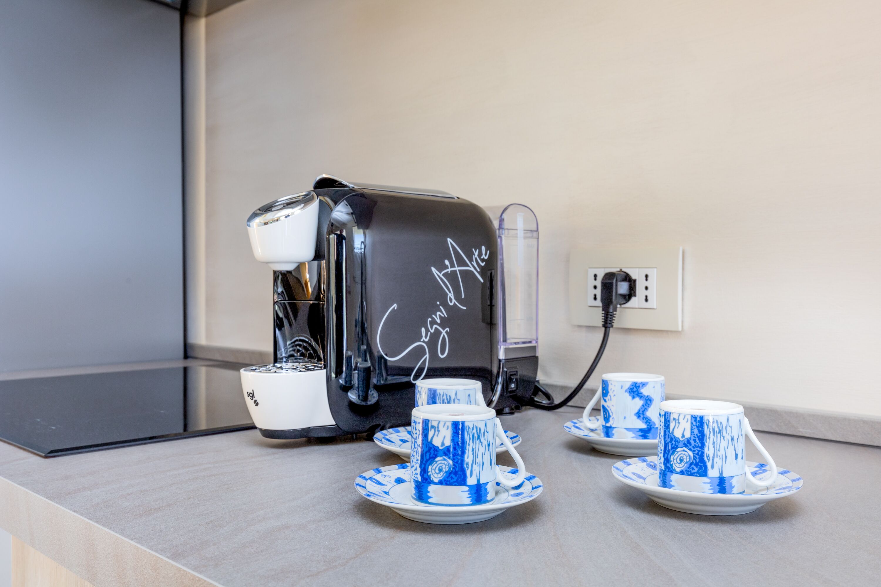 A coffee maker with a handwritten sign, two matching cups and saucers on a countertop.