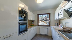 A modern kitchen with white cabinets, stainless steel appliances, a window with a view of a house, and a built-in oven.