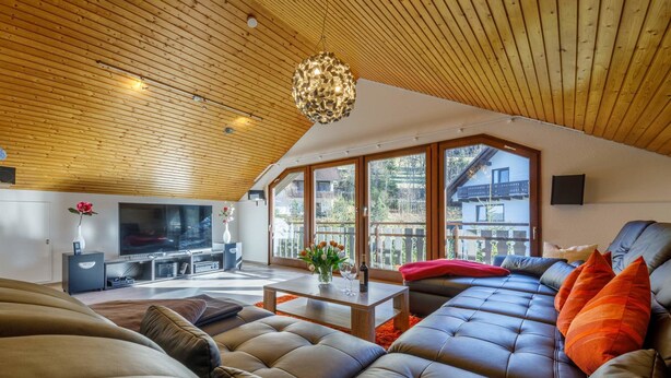 A spacious living area with a high ceiling, a large sofa set, a television, and a dining table.