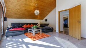 A modern living room with a wooden ceiling, a black leather sofa, a coffee table, and a door leading to another room.