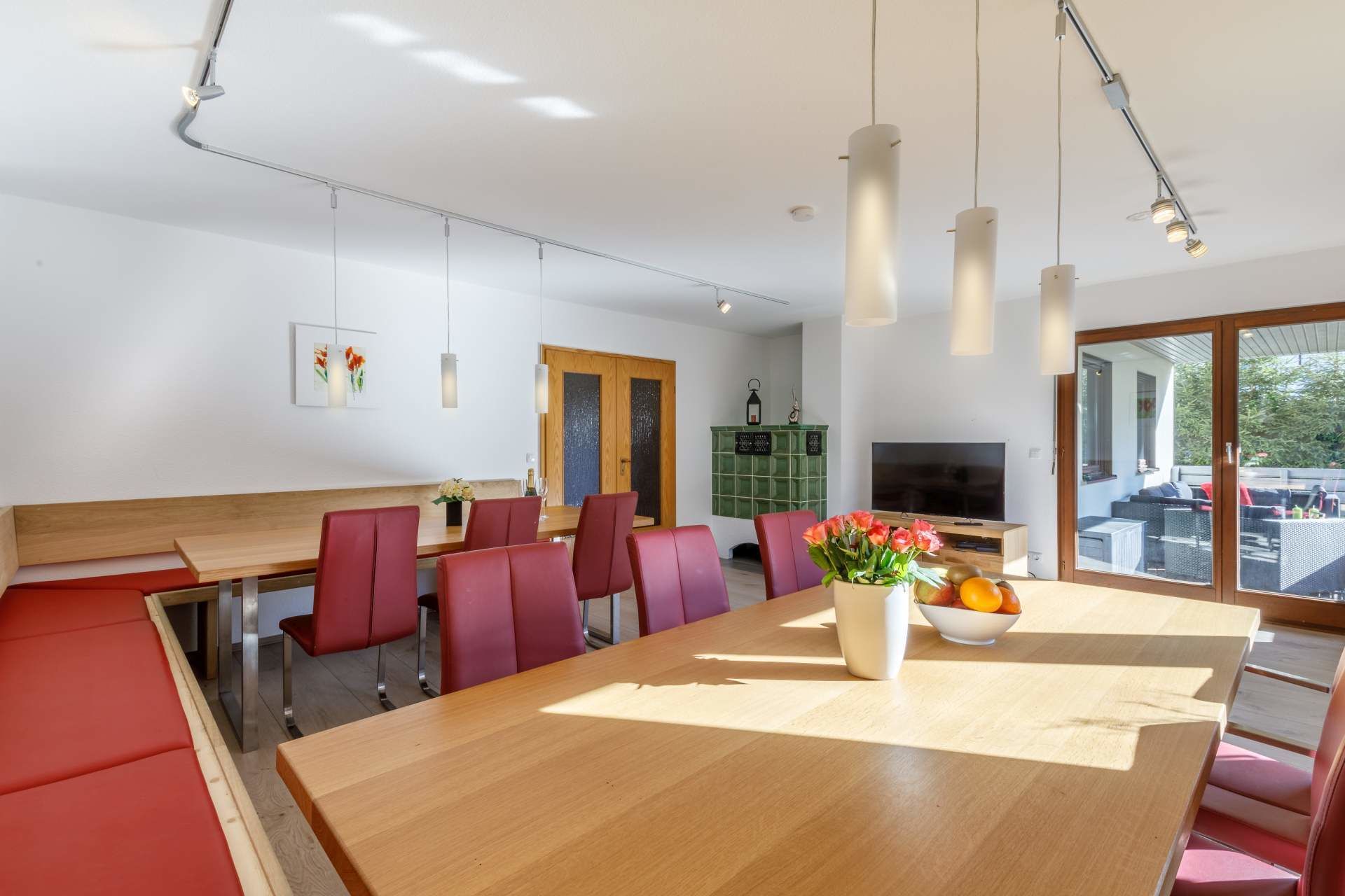 A modern dining area with a wooden table and red chairs, a TV, and a view of the outdoors.
