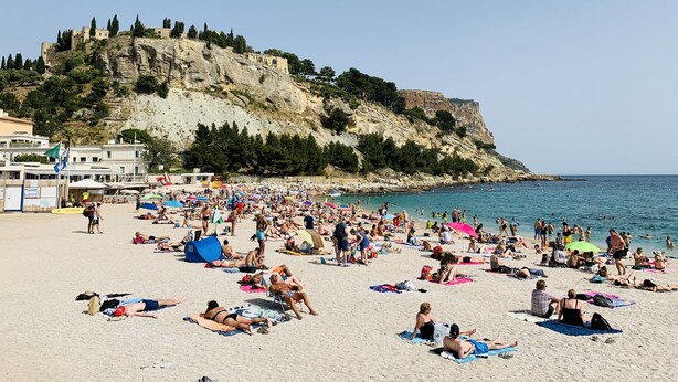 A crowded beach with people sunbathing and swimming, a rocky cliff in the background, and a clear blue sky. - L'ARENE Cassis Centre - T2 comfortable quiet 100m beach 4.5 kms calanques (Cassis)