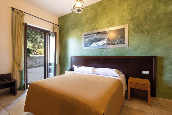 A hotel room with a bed, a nightstand, a bench, and a view of the outdoors through a glass door.