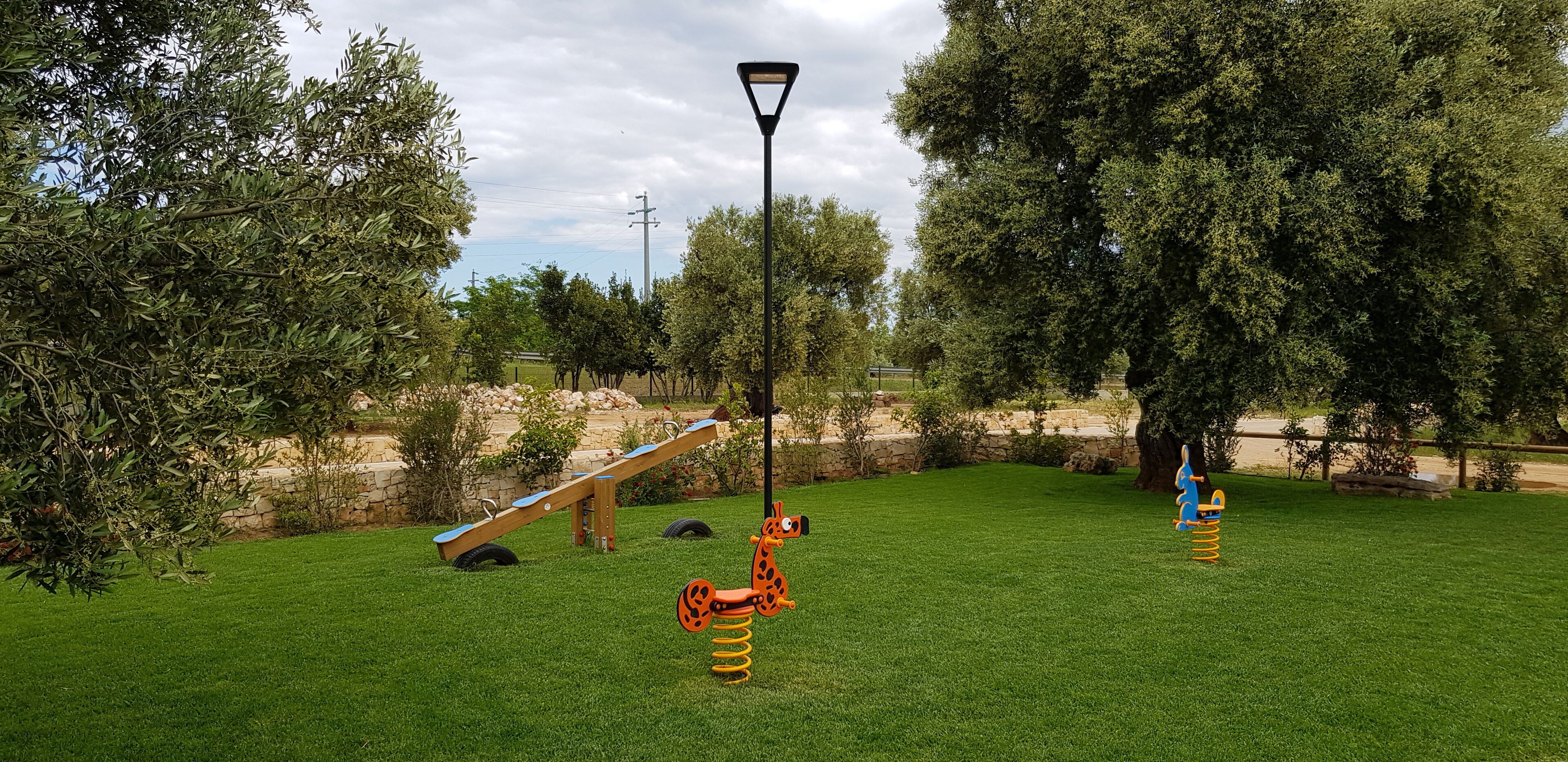Un área verde bien cuidada con juegos infantiles, que incluye un balancín, un columpio de jirafa y un caballito que rebota.