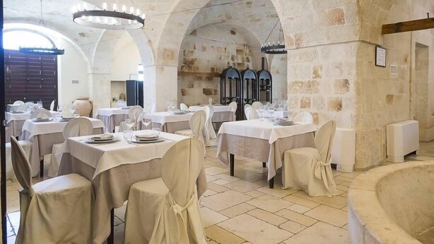 Un comedor con mesas dispuestas para el servicio, paredes de piedra y un amplio arco.
