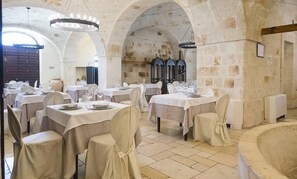 Un comedor con mesas dispuestas para el servicio, paredes de piedra y un amplio arco.